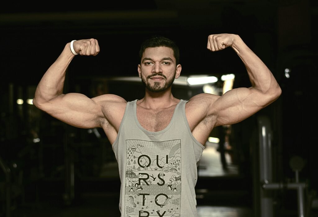 A fit man flexing his biceps in a gym environment, showcasing strength and fitness.